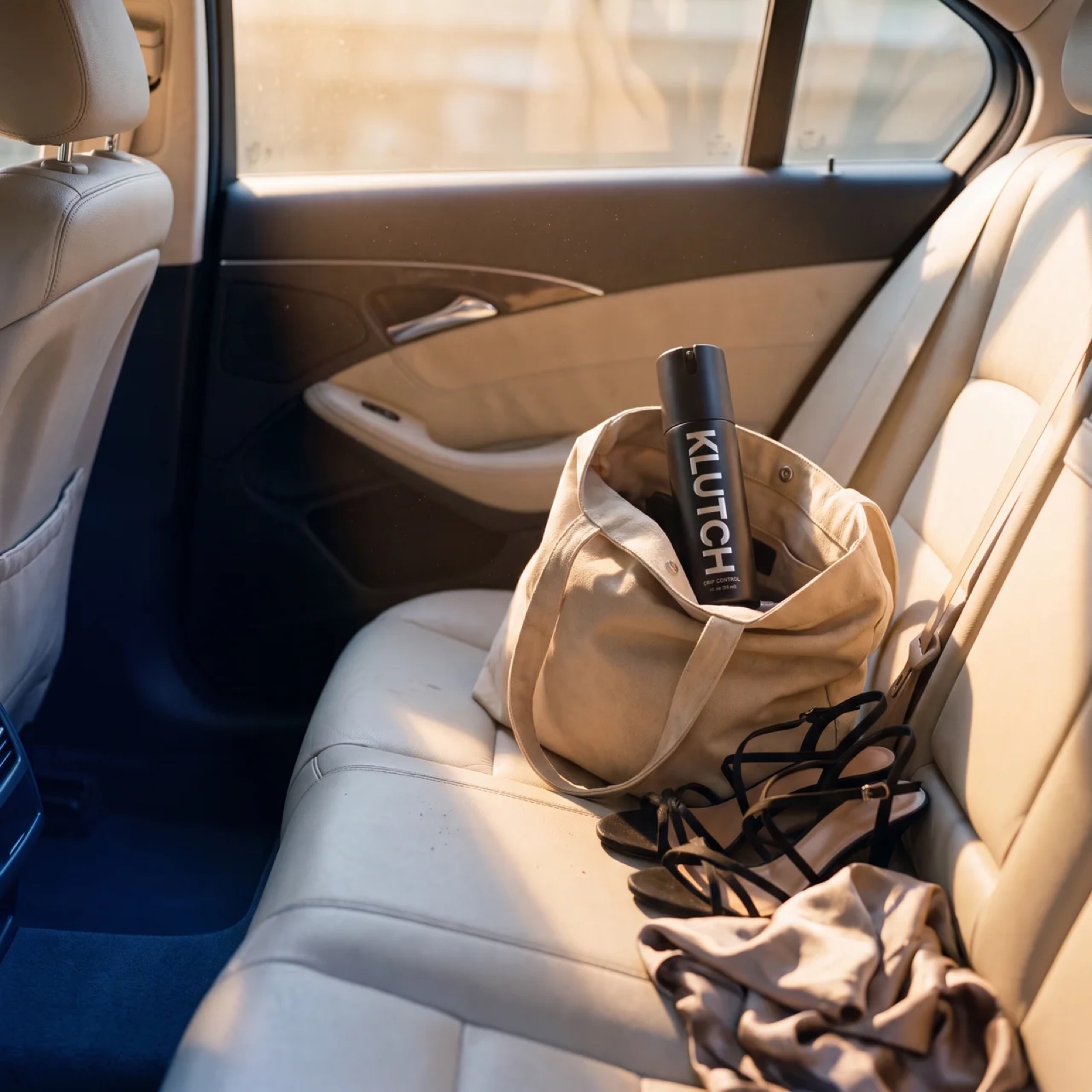 Klutch bottle in a tote bag on a car back seat with heels beside it