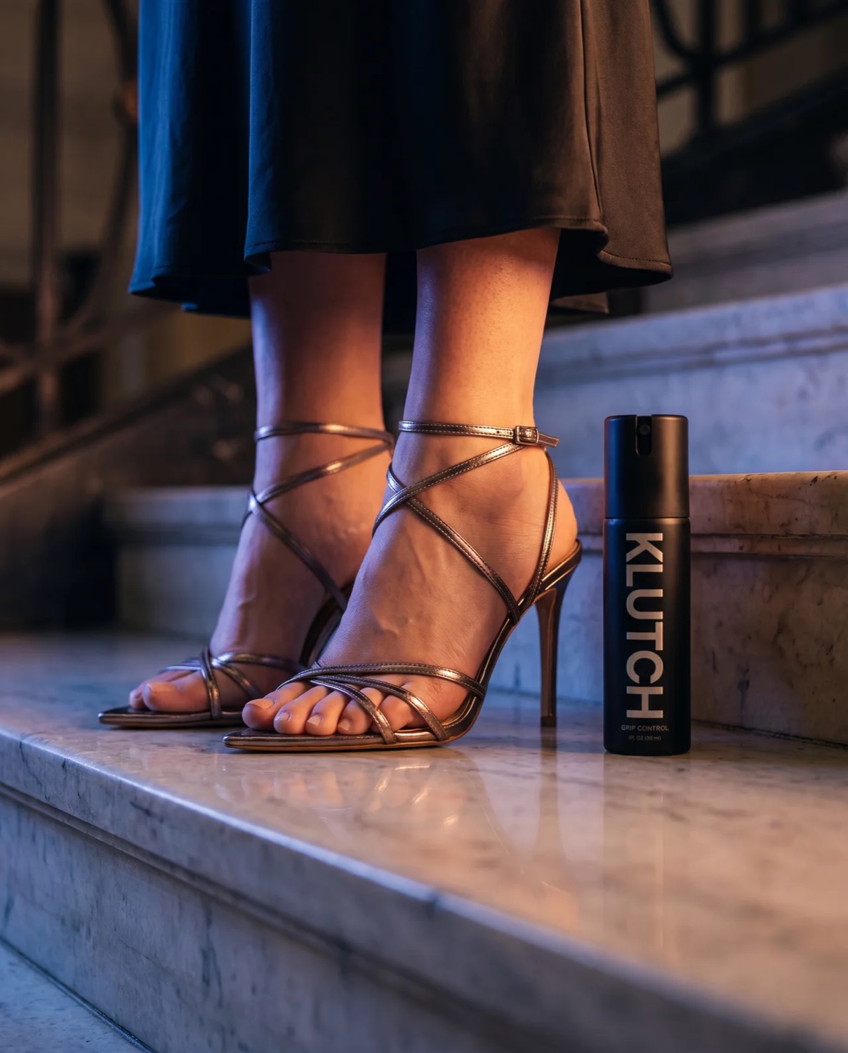 Metallic strappy heels on marble steps beside the Klutch bottle